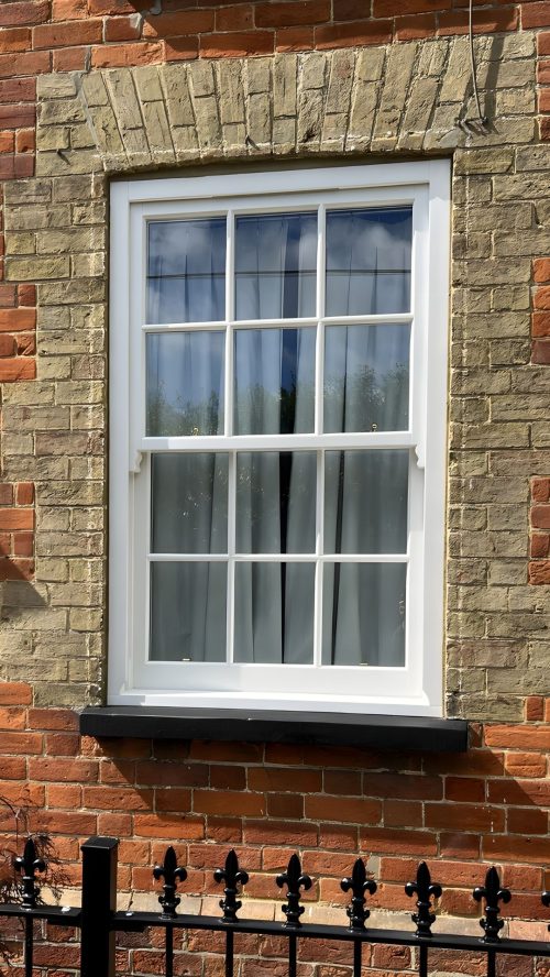 What Are Glazing Bars? Timber sash window with astragal glazing bars in a Georgian six-over-six layout, installed in a red and buff brick period property.
