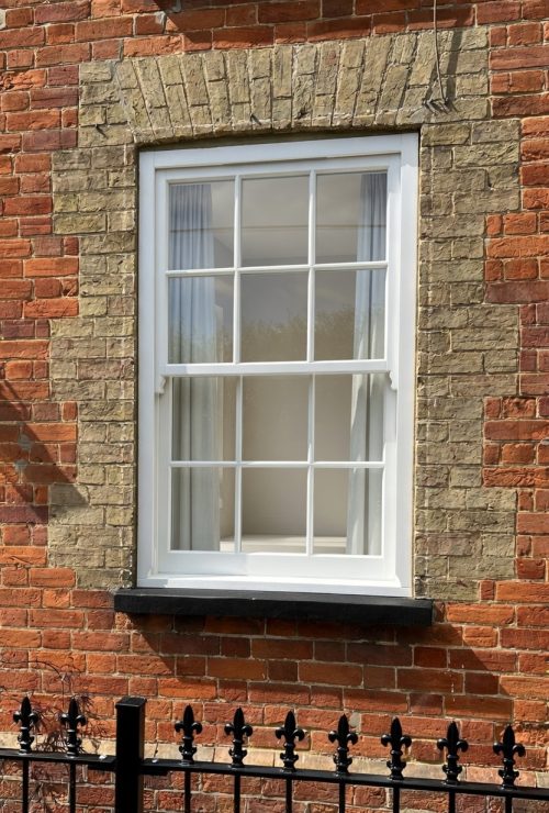 Timber sash window with astragal glazing bars in a Georgian six-over-six layout, installed in a red and buff brick period property.